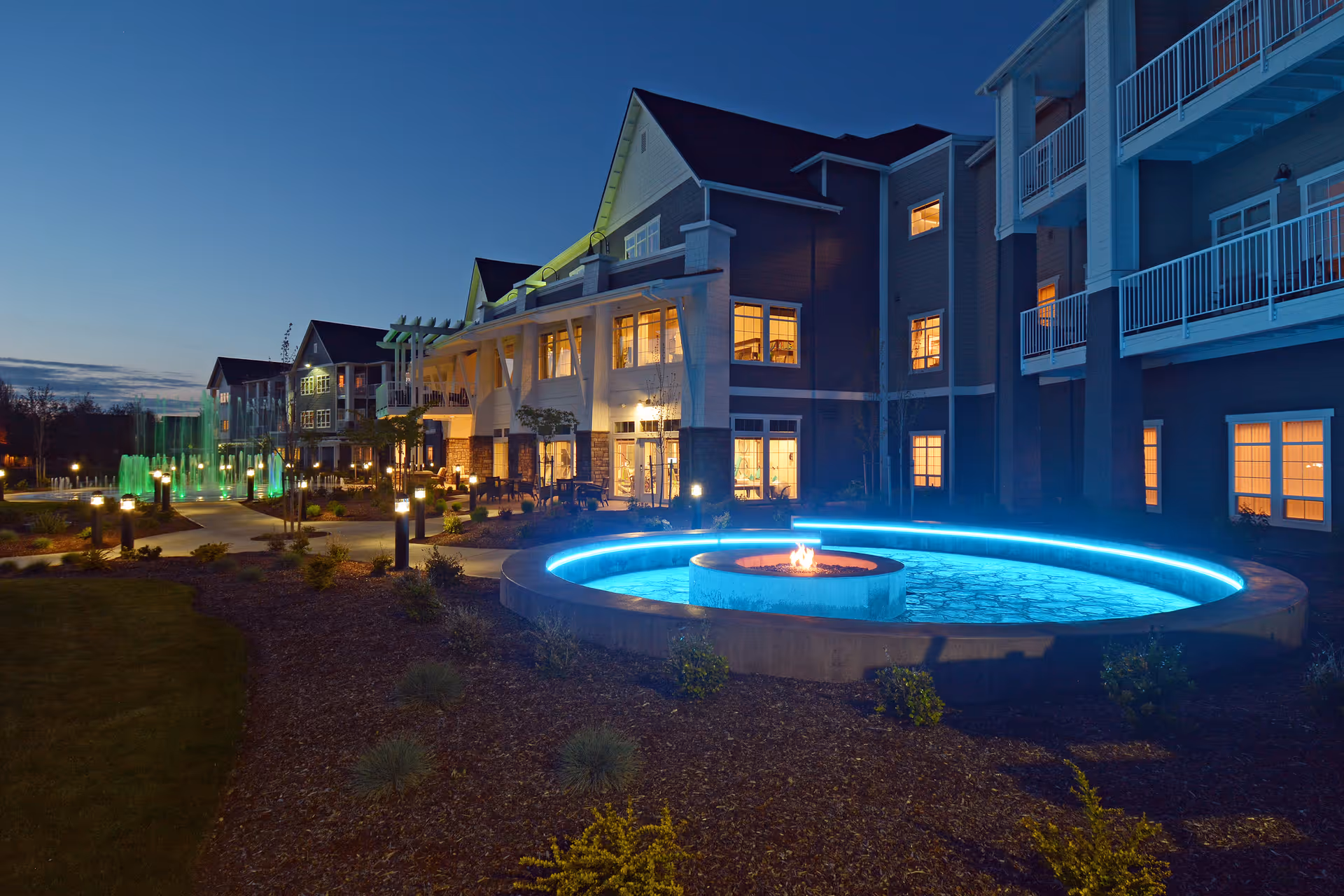Exterior front of the Waterford Grand at dusk featuring a lit circular fountain with a fire pit and the building's illuminated windows and balconies.