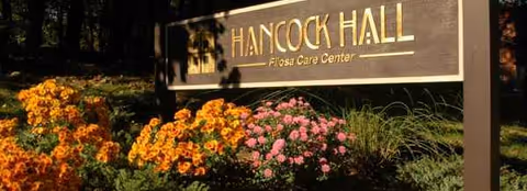 Exterior sign reading Havencare at Hancock Hall, with orange and pink flowers in front.