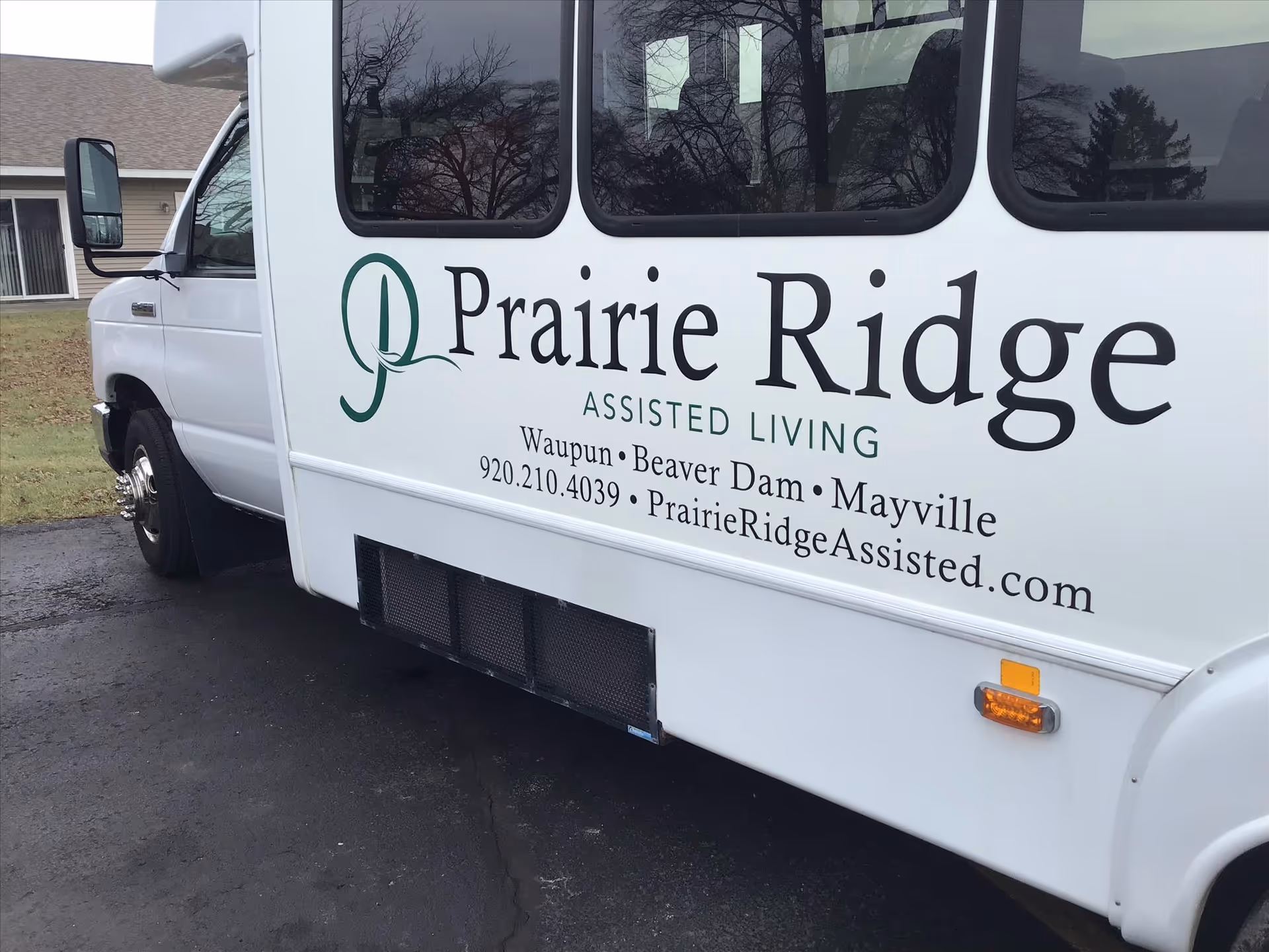Side of a Prairie Ridge Assisted Living shuttle van parked outdoors showing the facility name, locations, and contact information.