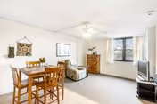Bright combined living and dining area with a wooden dining table and chairs, a recliner, dresser, TV, and a window with curtains.