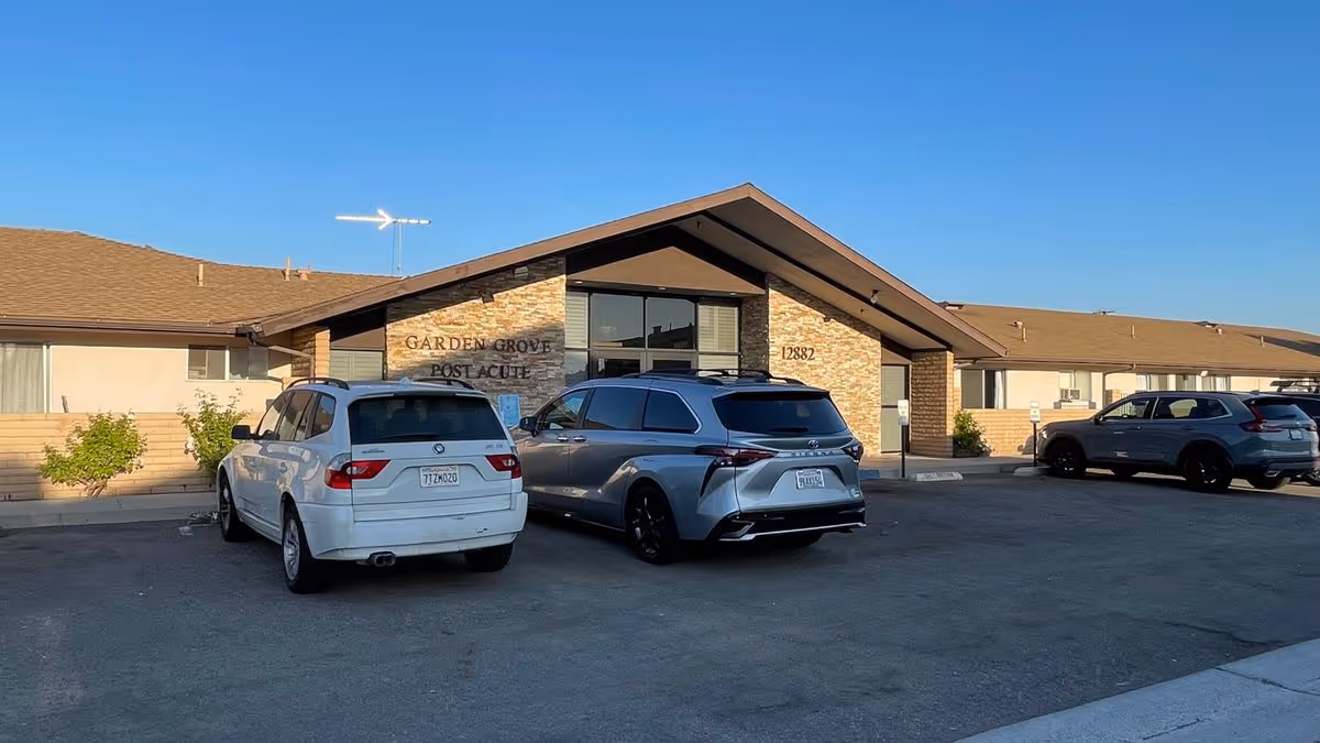 One-story brick-and-wood senior living facility entrance reading "Garden Grove Post Acute" with several cars parked in front.
