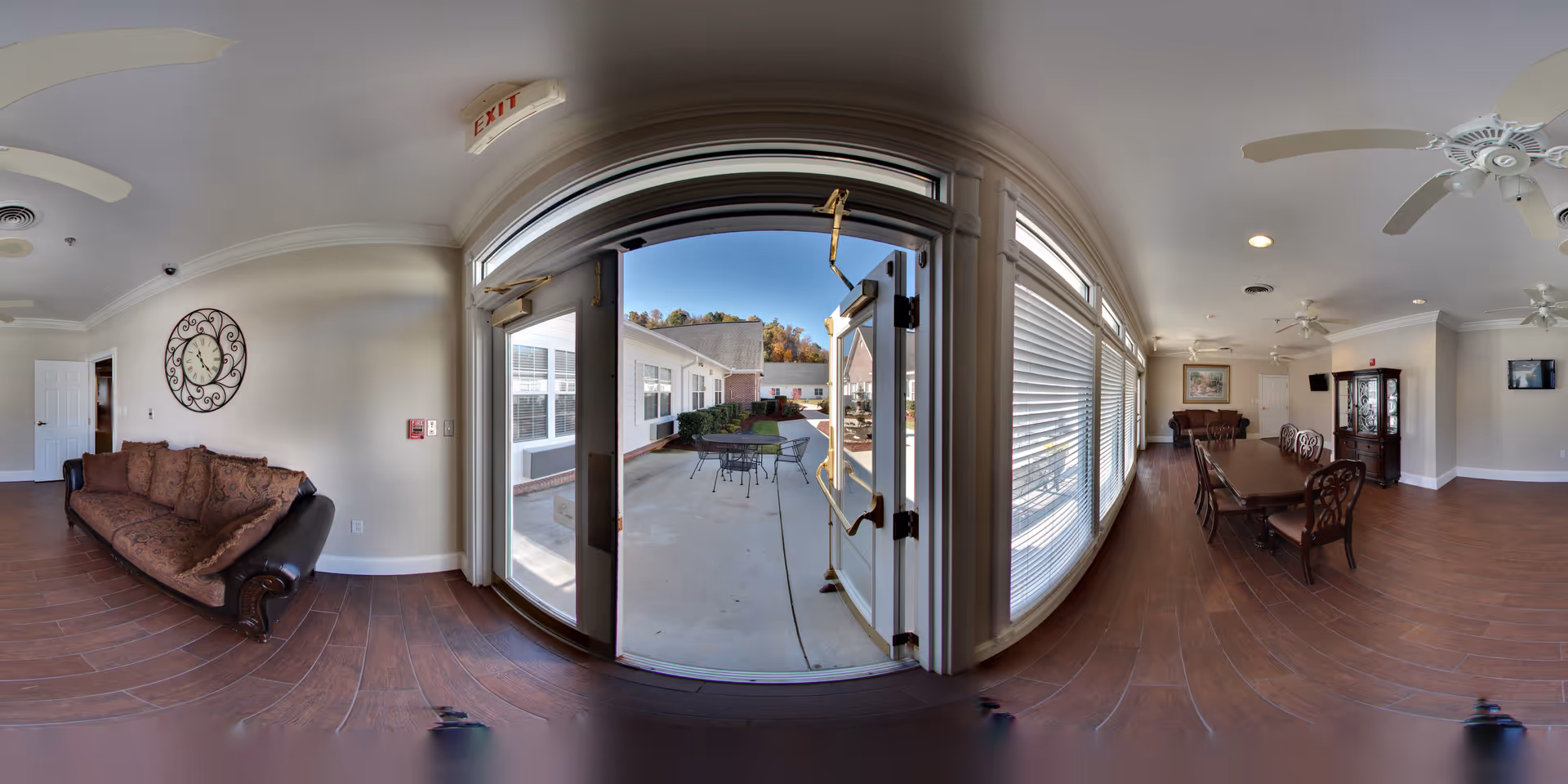 Spacious senior living common room with a sofa, long dining table and chairs and double doors opening to an outdoor patio.