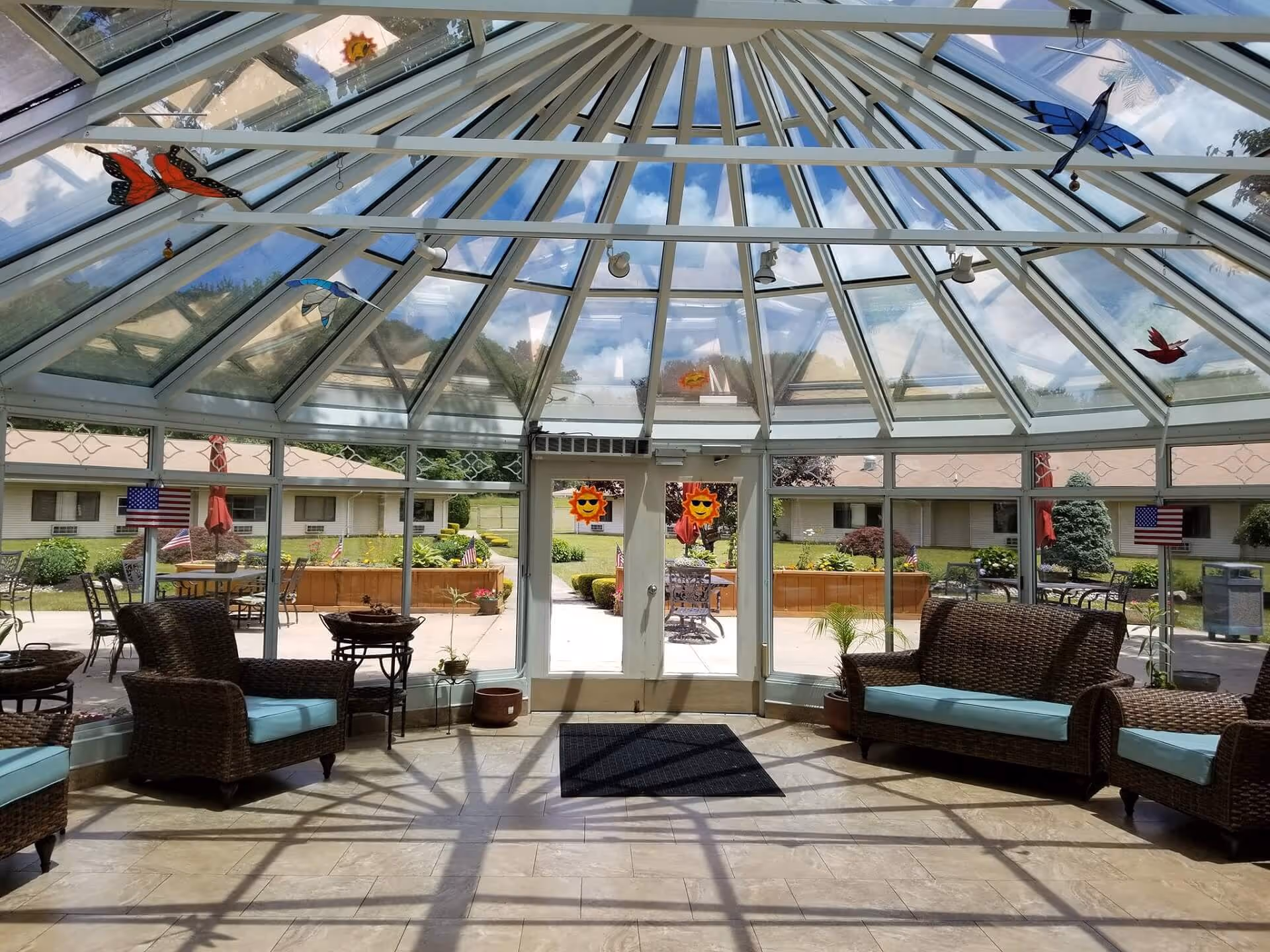 Glass-enclosed sunroom with wicker couches and chairs and a view of an outdoor patio.