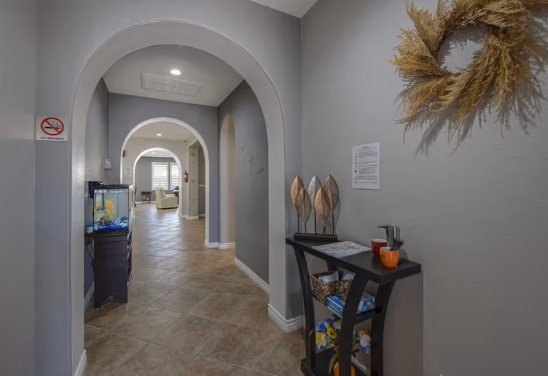 Interior hallway with tiled floor and arched doorways, a small console table and fish tank leading to a seating area.