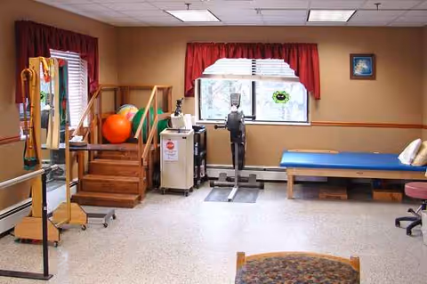 Senior living rehab room with exercise equipment, a blue therapy bed, and a red-curtained window.