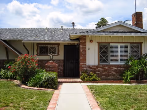 Front exterior of a single-story brick-and-siding house with a walkway, lawn, and shrubs.