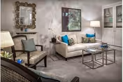 Cozy living room with a white sofa, two armchairs, two nested coffee tables, a decorative mirror and built-in cabinets.
