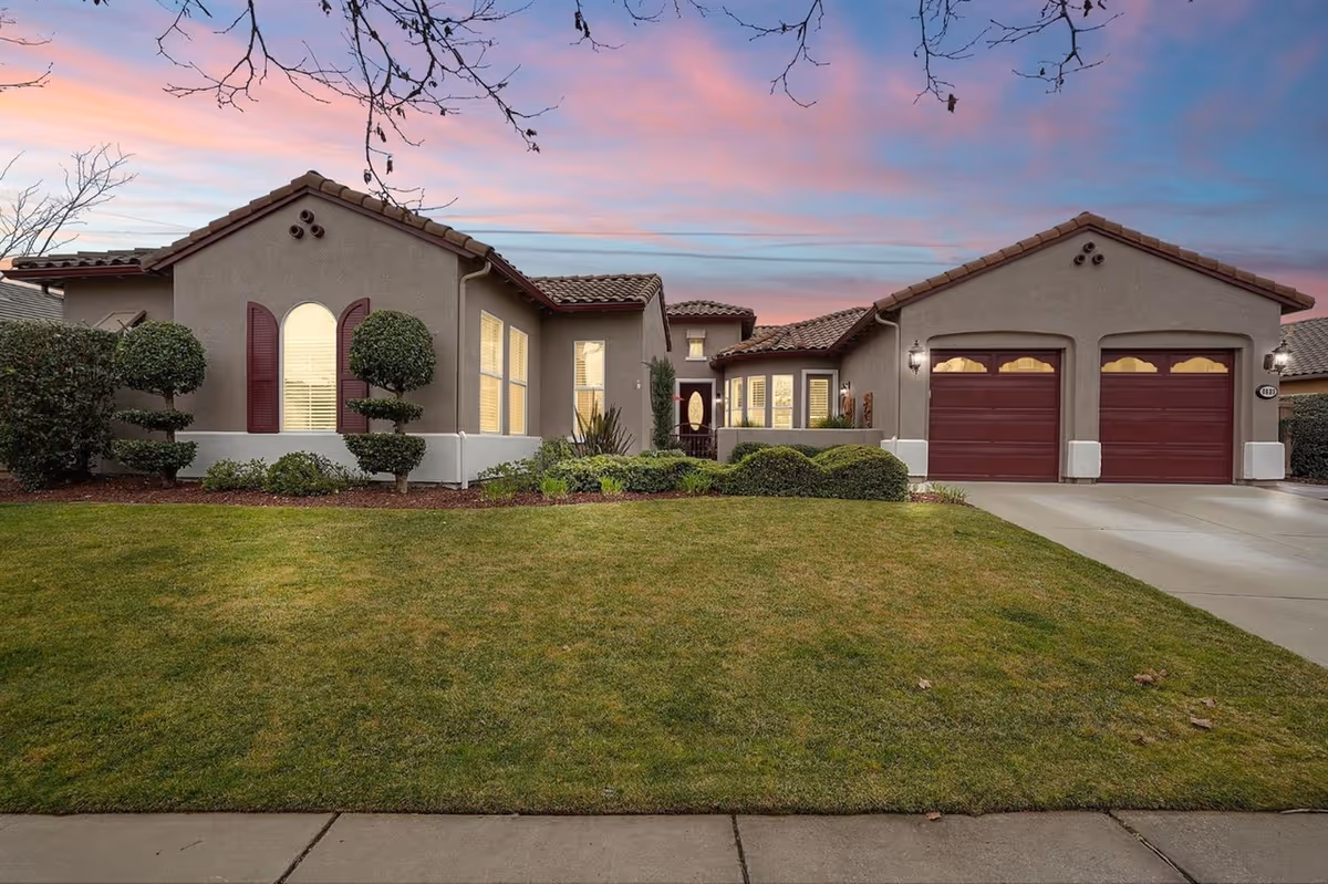 Exterior front view of a single-story residential building with a well-maintained lawn and neatly trimmed bushes, under a colorful sunset sky.