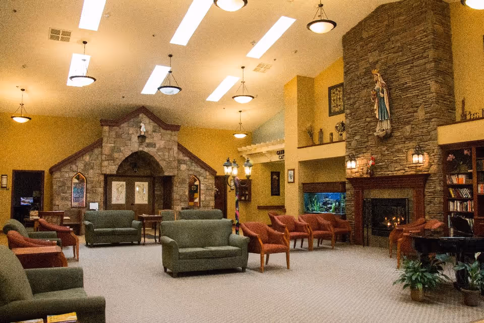 Spacious common room with sofas and armchairs arranged around a stone fireplace and decorative stone arch.