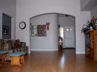 Cozy living room area in a senior facility with sofa, chair, clock, and doorway.