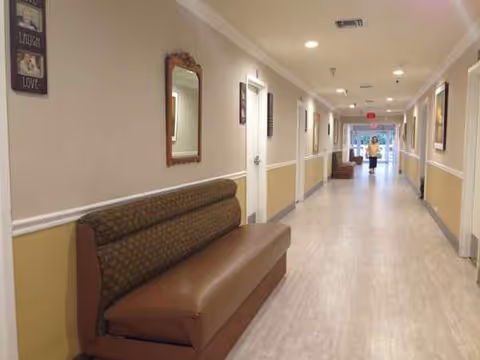 Long beige hallway of a senior living facility with seating and framed mirrors.