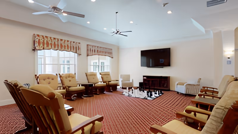 Common living room with upholstered armchairs arranged in a circle around a rug facing a wall-mounted TV.