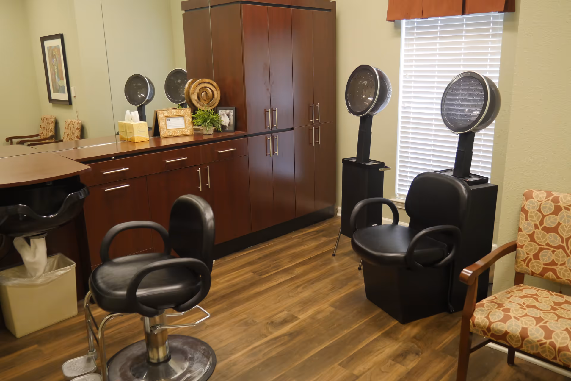 A small salon-style room with styling chairs, hooded hair dryers, and wooden cabinets against a wall.