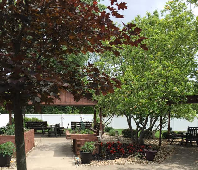 Shaded outdoor courtyard with trees, raised planter beds, benches and patio tables under wooden pergolas.