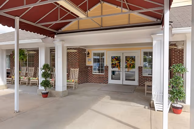 Covered brick entrance with double glass doors, rocking chairs, and potted plants at the facility entrance.