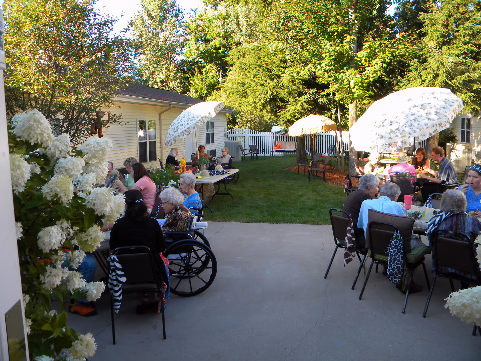 Seniors gathered outdoors in a courtyard/patio with tables, umbrellas, and a nearby building.