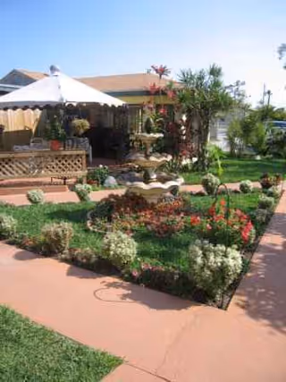 Outdoor garden patio with colorful flower beds, walkway, and shaded seating area.