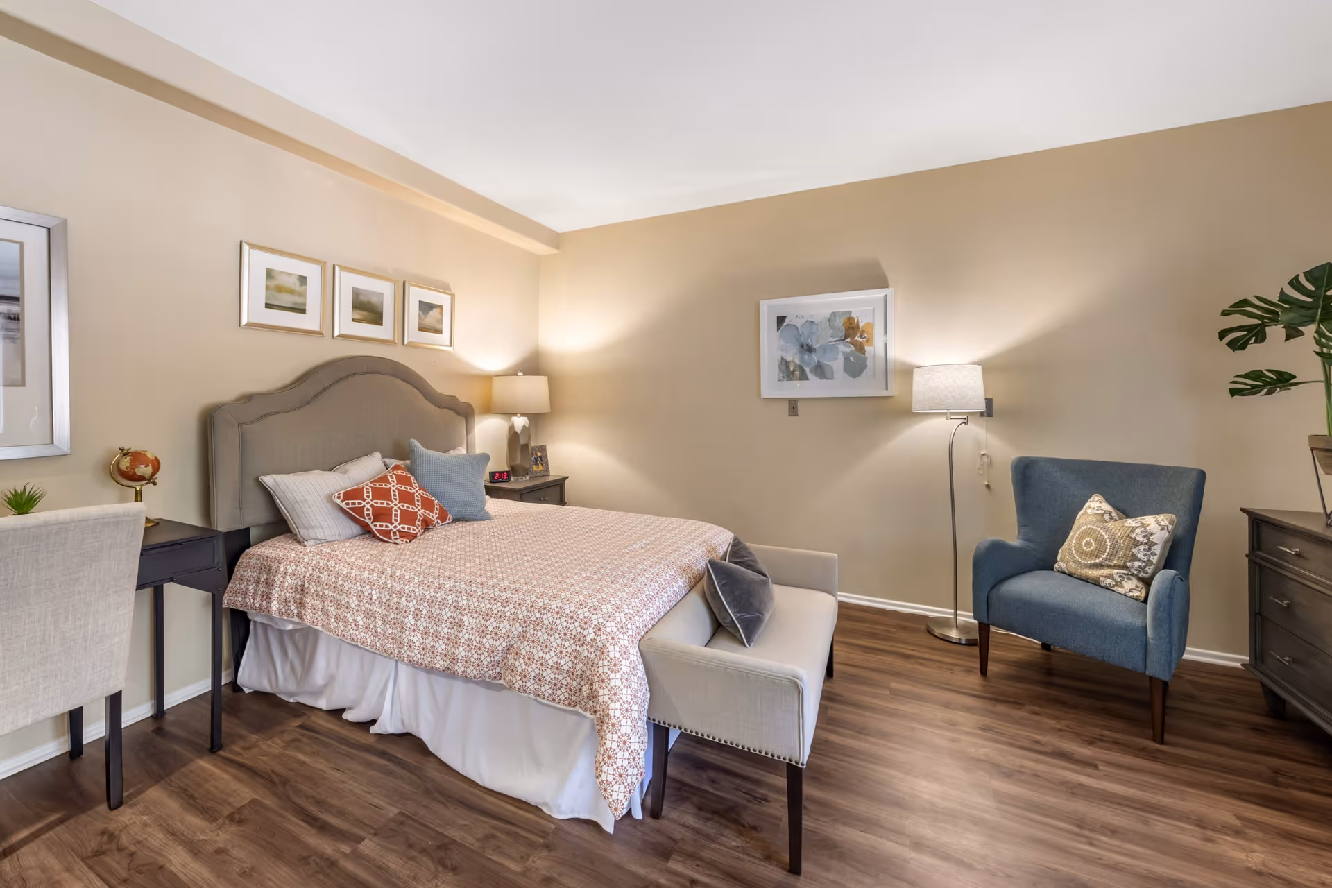 Well-lit furnished bedroom with a bed, upholstered headboard, bench at the foot, armchair, nightstands and lamps.