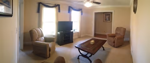Cozy living room with reclining chairs, a coffee table, TV, and two windows letting in light.