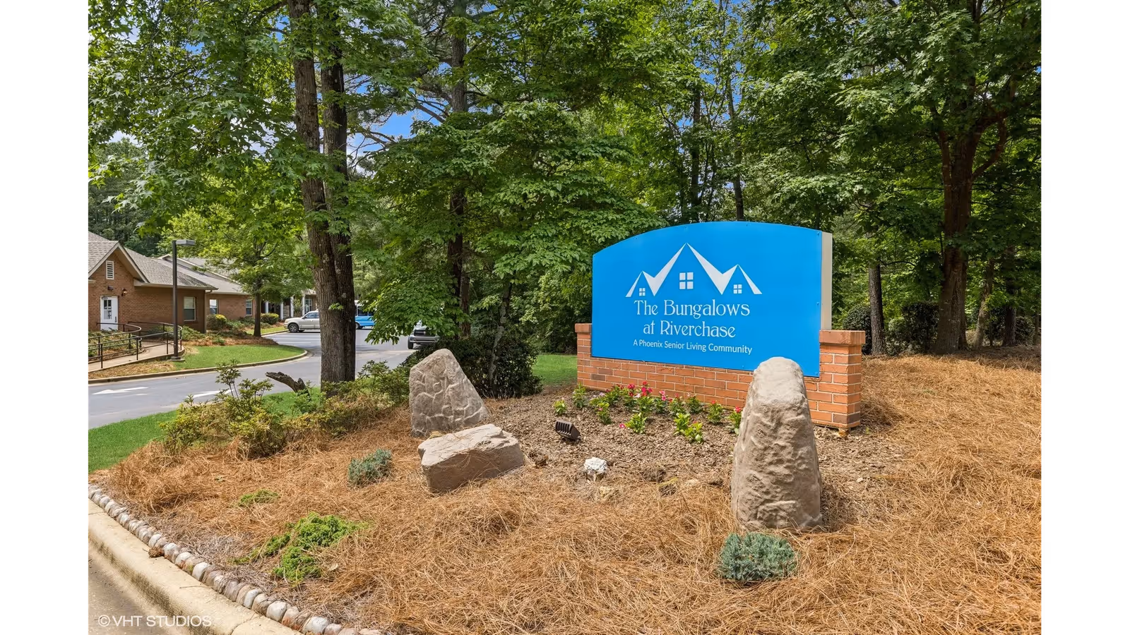 Entrance sign for The Bungalows at Riverchase on a landscaped bed with trees and nearby buildings.