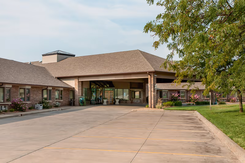 Front entrance of a single-story brick senior living facility with a covered porte-cochère and empty parking area.
