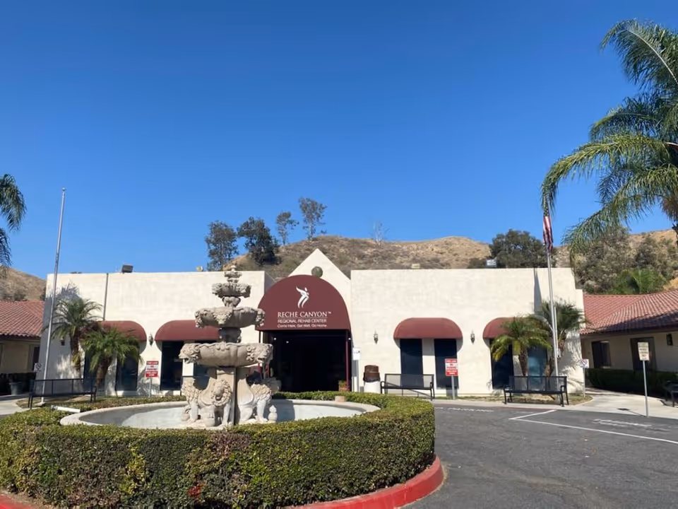 Front view of Reche Canyon Regional Rehab Center with a fountain, curved driveway, and palm trees.