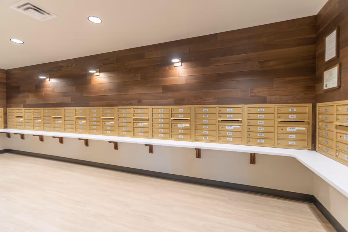 Interior mailroom with rows of gold apartment mailboxes mounted on a wood-paneled wall above a white countertop.