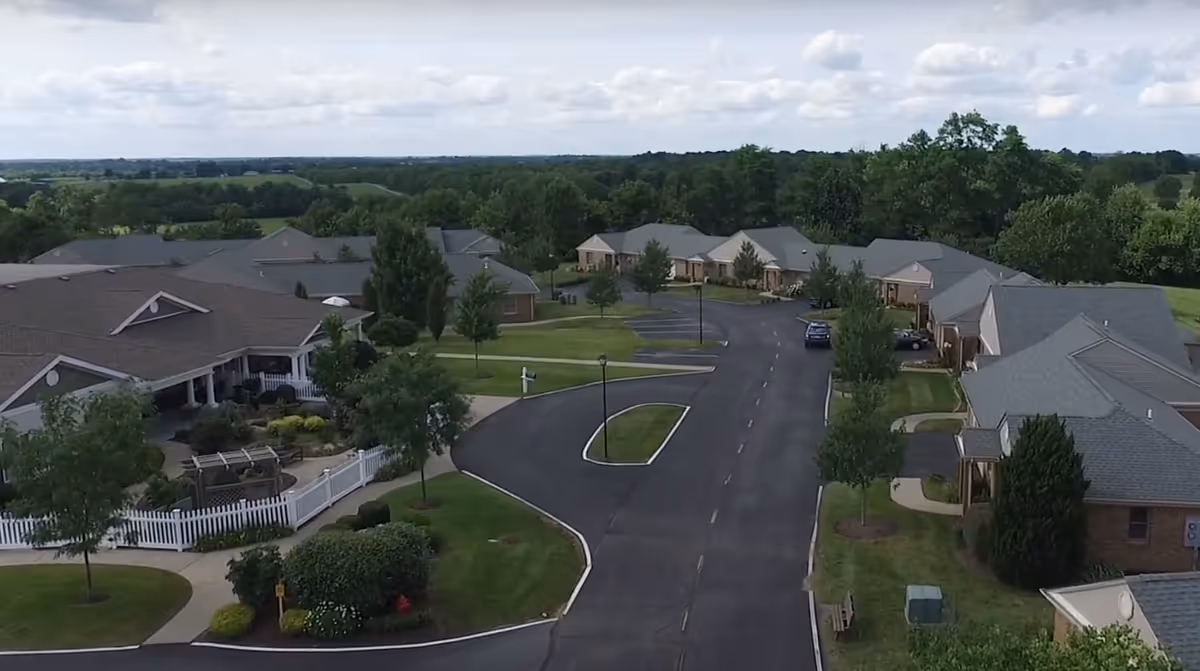 Aerial view of the Wesley Village Senior Living campus with single-story residences, a curved driveway, lawns and trees.