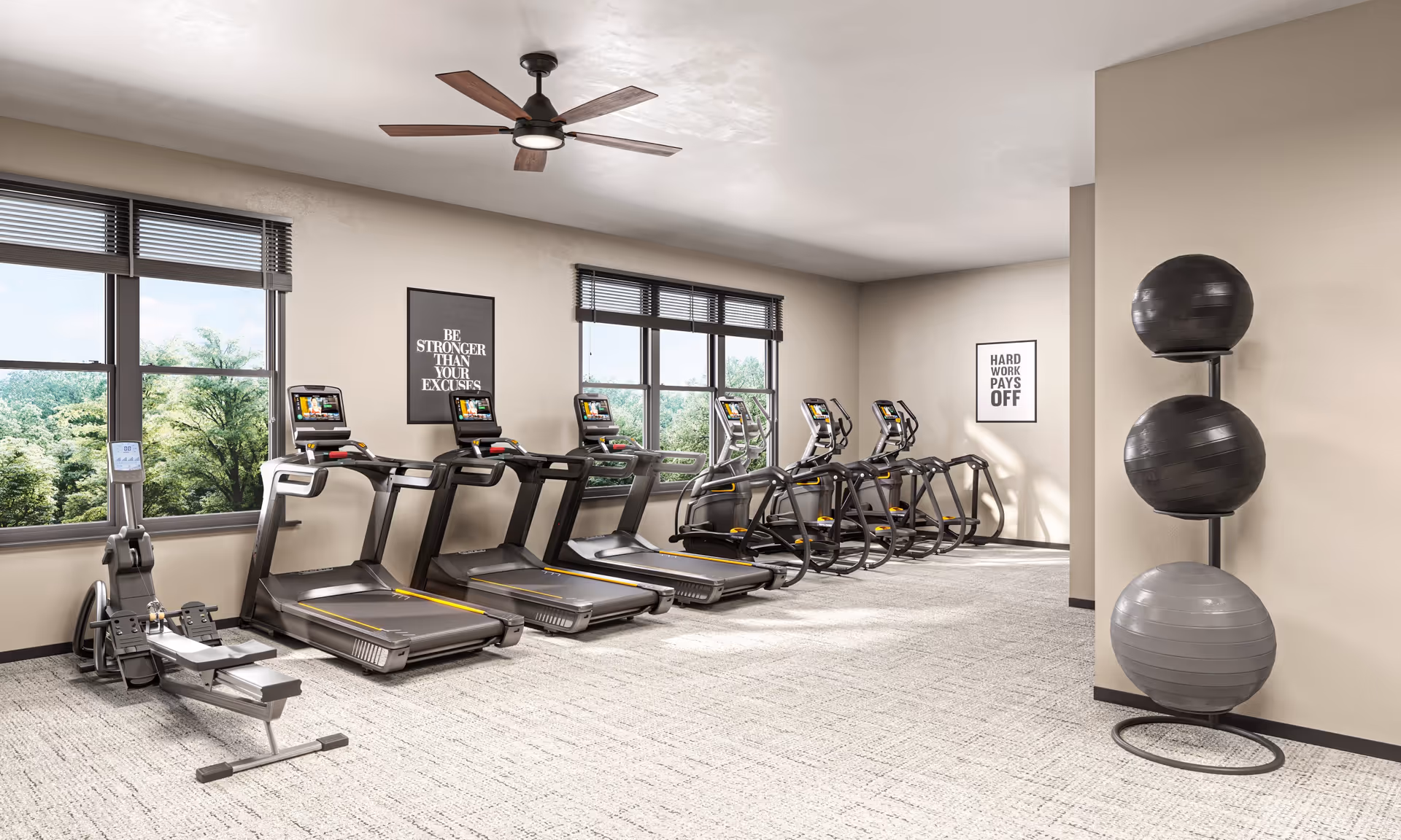 A bright fitness room with several treadmills, elliptical machines, and a rowing machine lined up against a wall with large windows showing green trees outside. There are two motivational posters on the walls that read 'BE STRONGER THAN YOUR EXCUSES' and 'HARD WORK PAYS OFF'. Three exercise balls are stacked on a vertical rack in the corner.