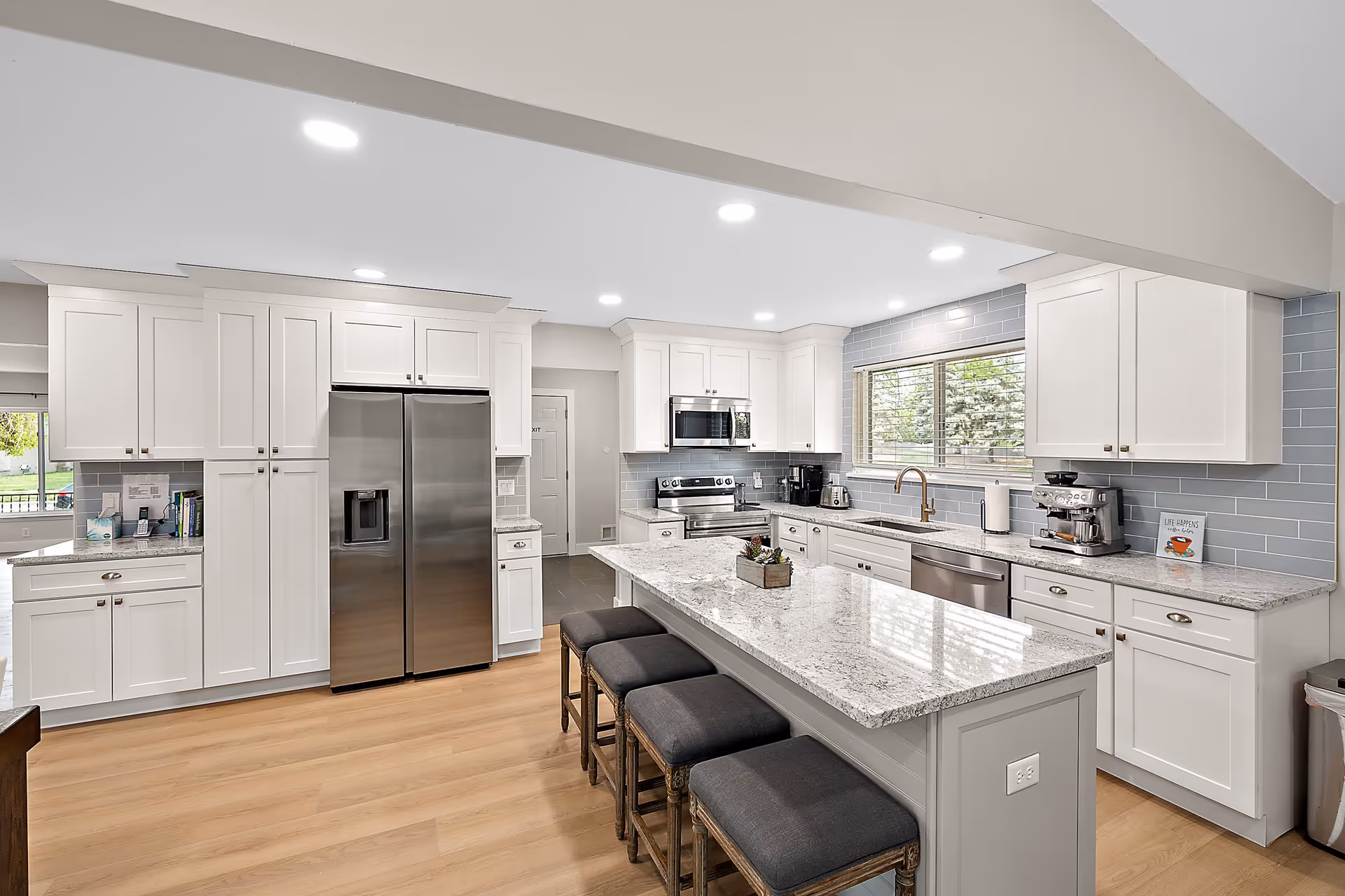Bright modern kitchen with a large marble island, white cabinets, stainless steel appliances, and bar stools.