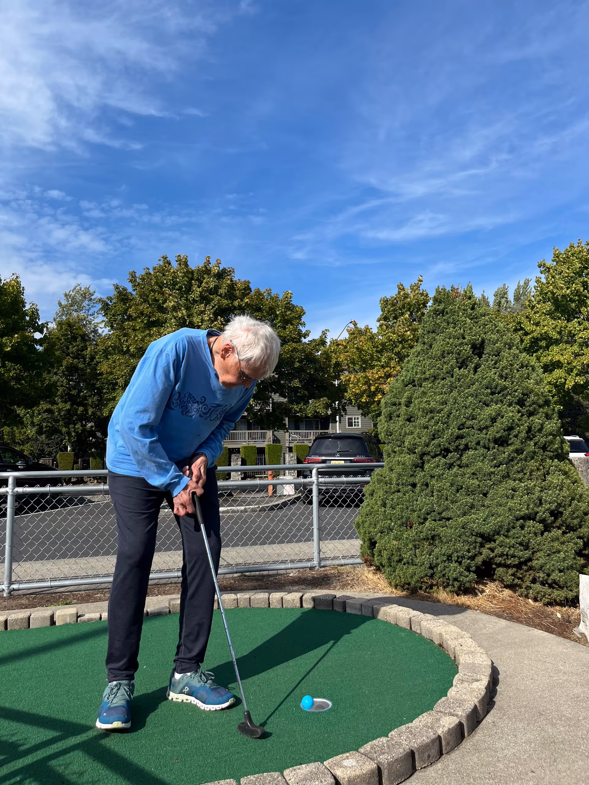 An elderly man playing mini golf outdoors on a sunny day.