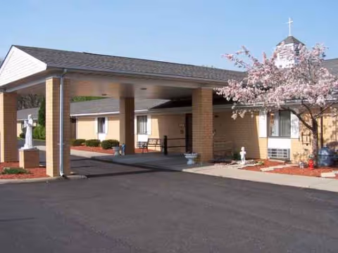 Exterior view of a senior living facility entrance with a covered drive and pink blossoms.