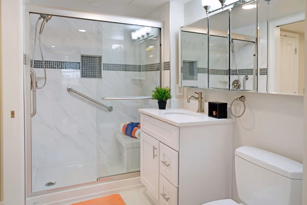 Bright accessible bathroom with a glass-enclosed walk-in shower with grab bars, white vanity, and toilet.