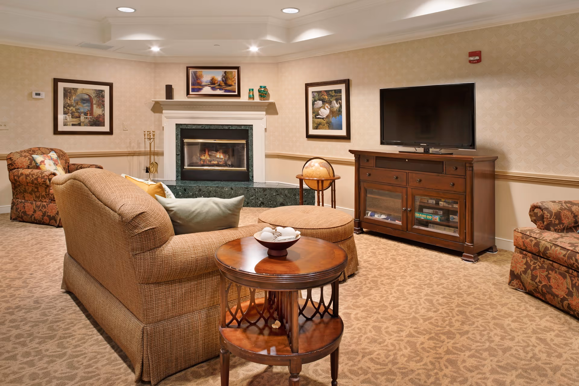 Cozy communal living room with a sofa, armchairs, fireplace, TV on a wooden console, and a round coffee table.