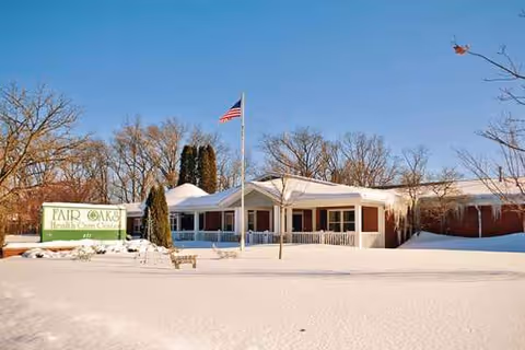 Exterior view of Fair Oaks Health Care Center with snow, flag, and sign.