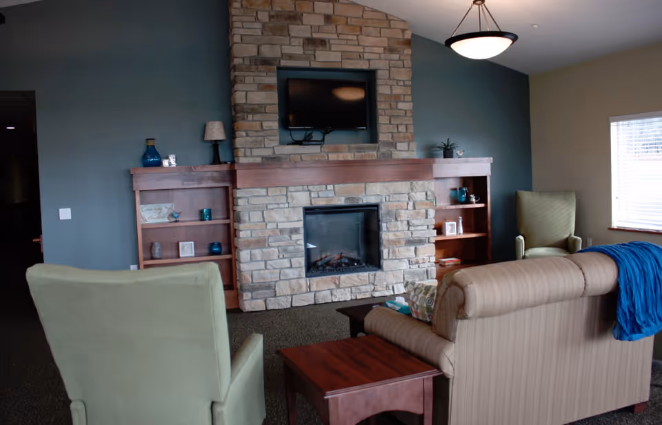 Cozy seating area with armchairs and a sofa facing a stone fireplace with built-in shelves and a mounted TV.