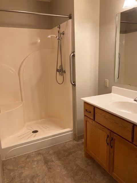 Small bathroom featuring a corner walk-in shower with a grab bar and a wooden vanity with sink and mirror.