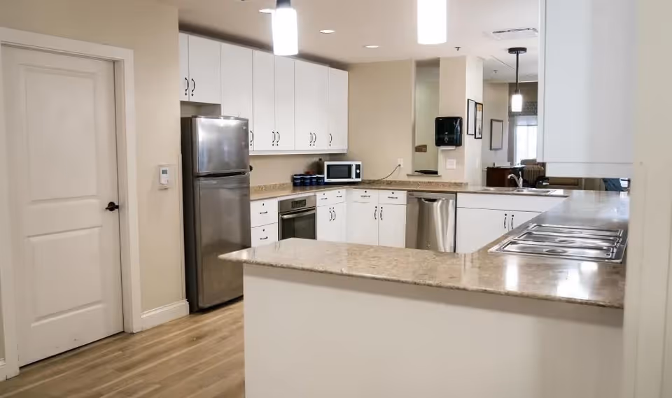 Bright open kitchen with white cabinets, stainless steel refrigerator and dishwasher, granite countertops and pendant lighting.