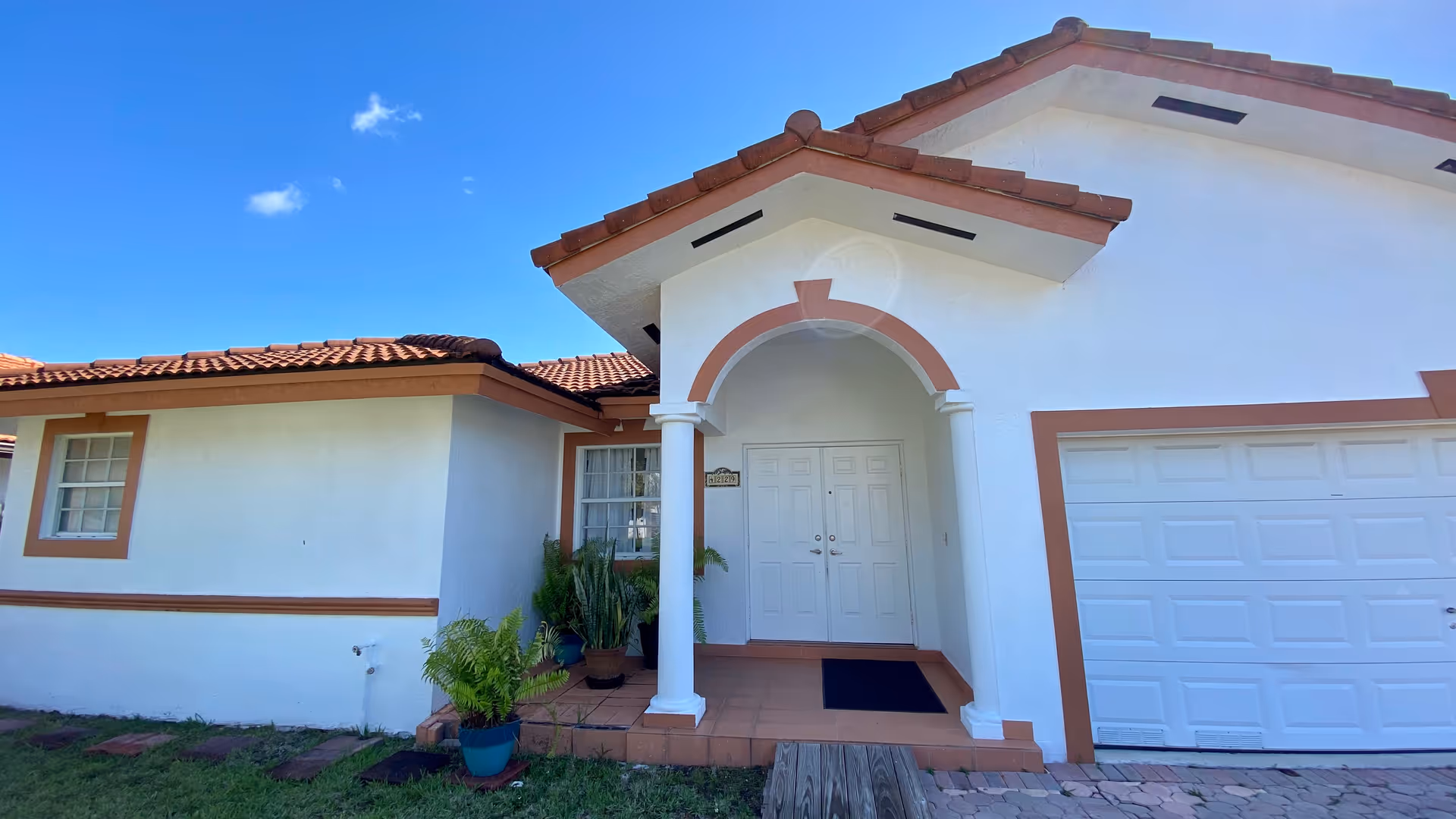 White stucco senior home with arched entry, columns, terracotta roof, and potted plants.