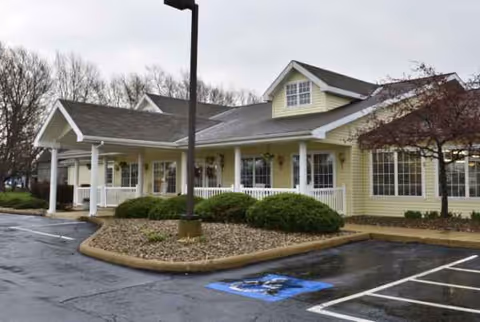 A yellow single-story senior living facility with a covered entrance and manicured shrubs.