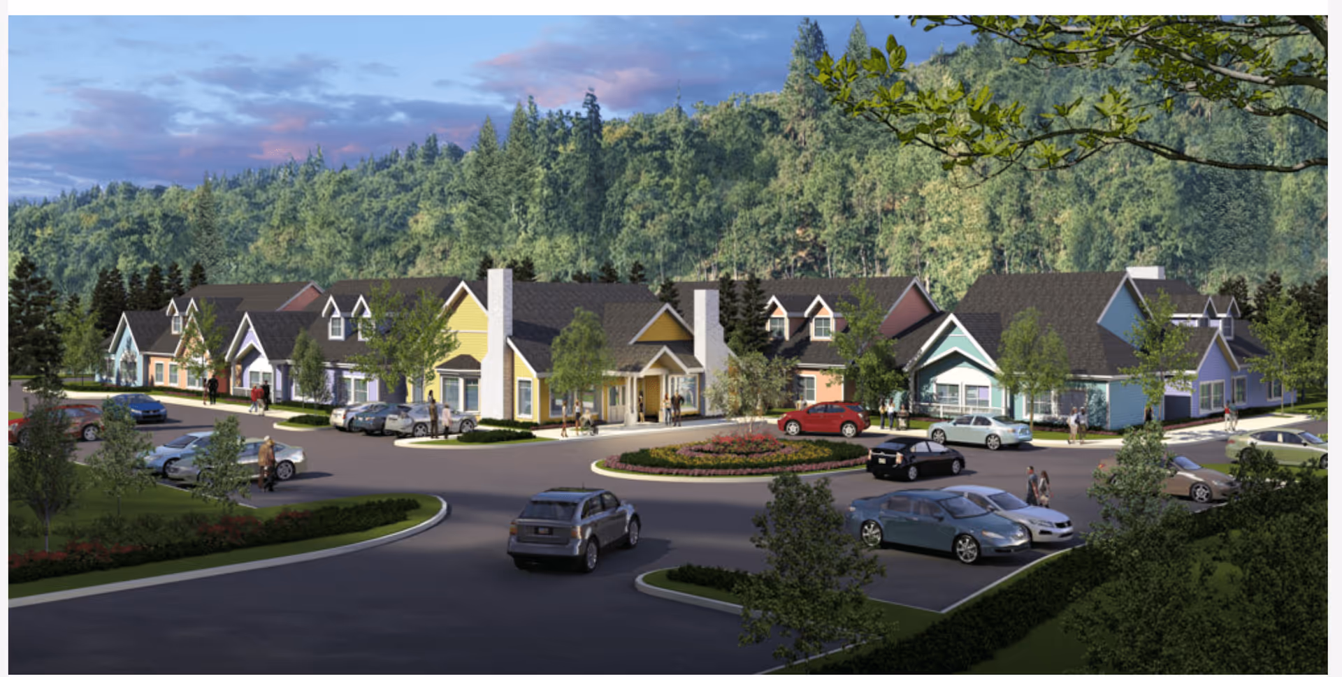 View of a senior living community with multiple colorful residential buildings surrounded by trees and greenery. Several cars are parked in the parking lot, and a few people are walking around the area. The background features a forested hillside under a partly cloudy sky.