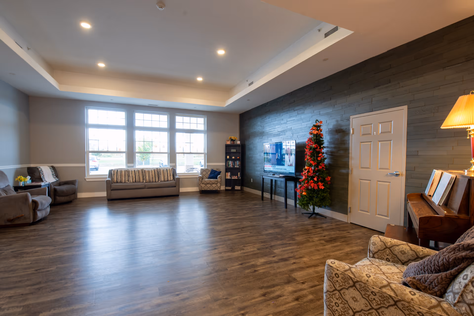 Spacious common lounge with sofas and armchairs, a TV, piano, and a decorated Christmas tree.