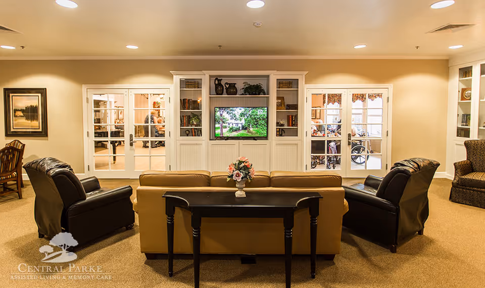 A cozy lounge with a sofa and recliners facing a built-in TV and shelving, with glass French doors behind.