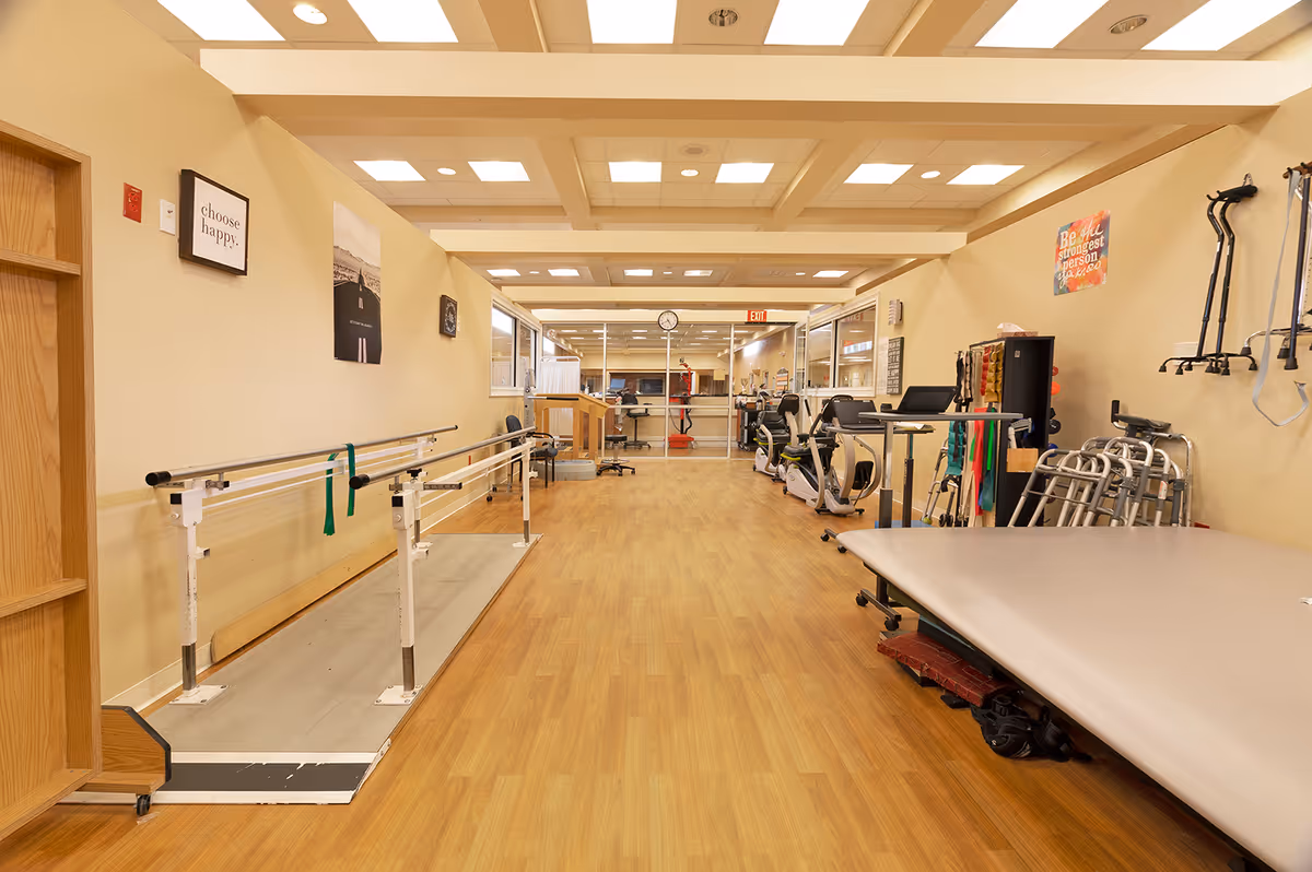 Rehabilitation/exercise room with parallel bars, exercise equipment, walkers and a treatment table.
