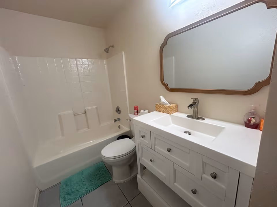 Small bathroom with a bathtub-shower combo, toilet, white vanity with sink and mirror.
