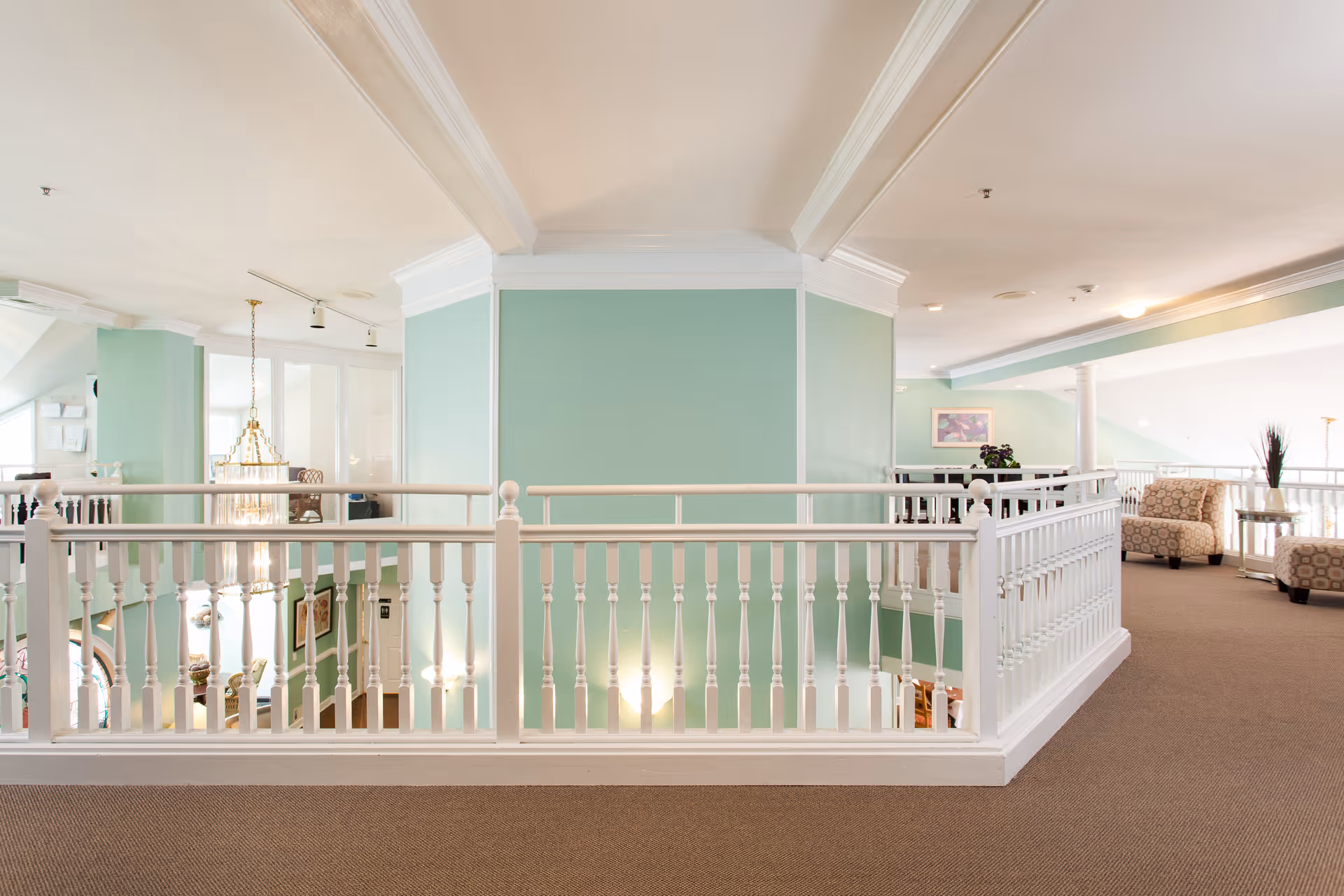 Bright second-floor interior hallway with white railing, mint-green walls, and seating areas.