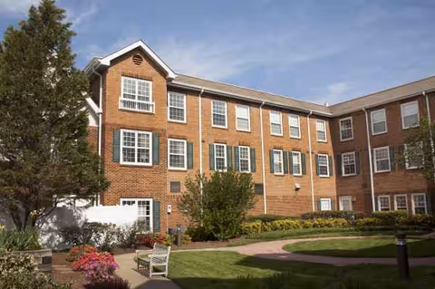 Brick exterior of The Rivers at Maryland Farms with windows, greenery, and a curved lawn path.
