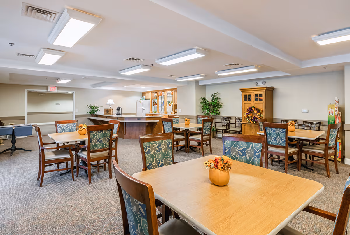 Communal dining room with multiple tables and chairs, a serving counter, and autumn decorations.