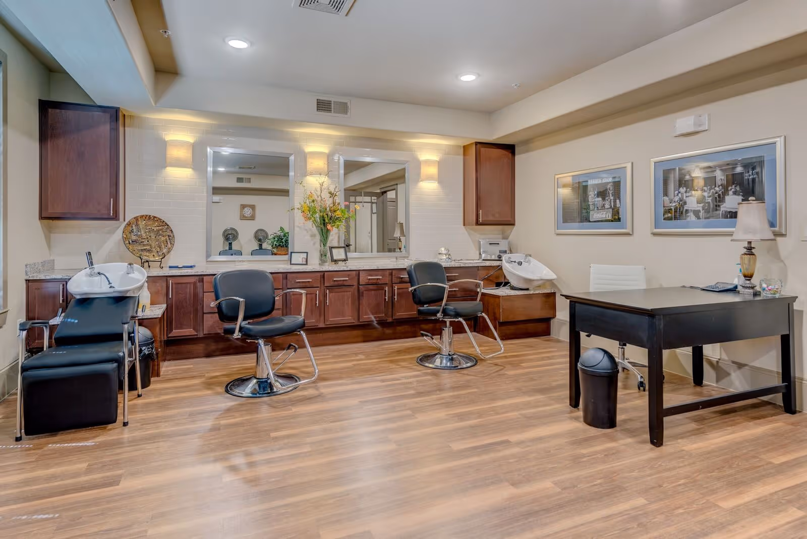Well-lit salon room with styling chairs, shampoo basins, large mirrors, wooden cabinets and a desk on wood flooring.