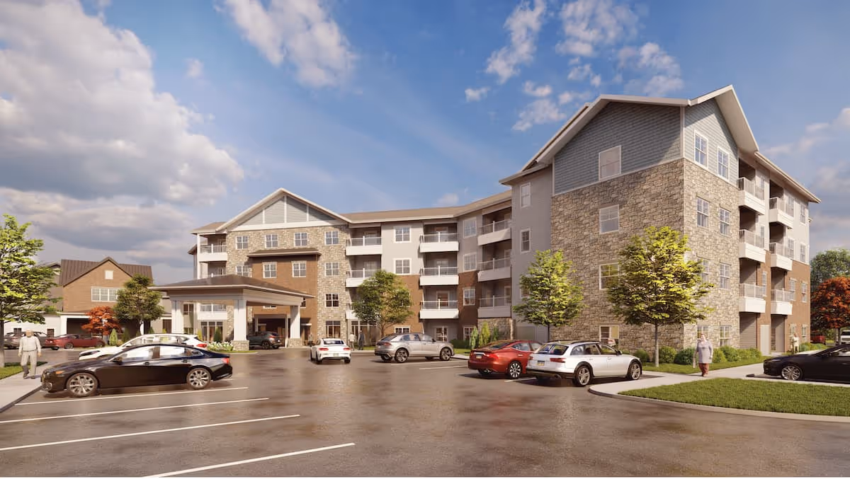 Exterior view of a multi-story retirement community building with stone and siding facade, balconies, a covered entrance, parked cars in the parking lot, and a few people walking on the sidewalks under a partly cloudy sky.